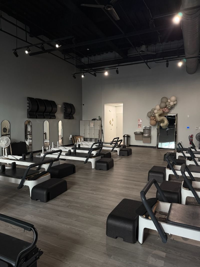 Pilates studio with reformers, gray walls, wood floors, and dark ceiling.