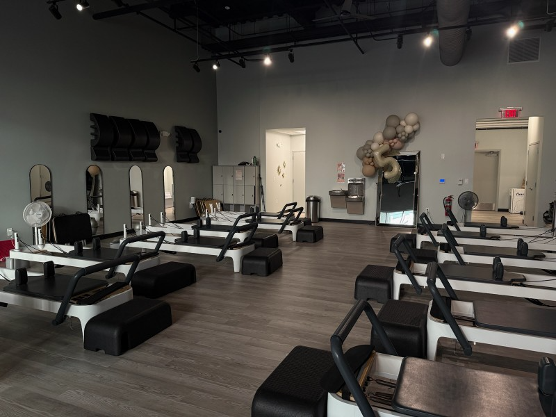 Pilates studio with exercise machines, mirrors, and gray walls.