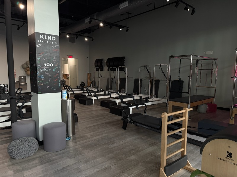 Pilates studio: Reformers, Cadillac, gray & black equipment. Light wood floor, neutral walls.