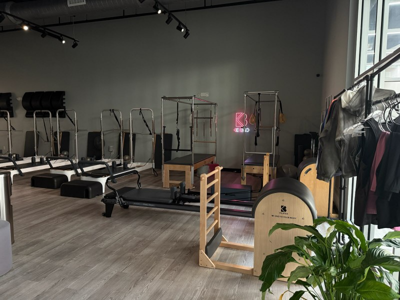 Pilates studio with specialized equipment, various stations set up, neutral tones, and a rack of clothing.
