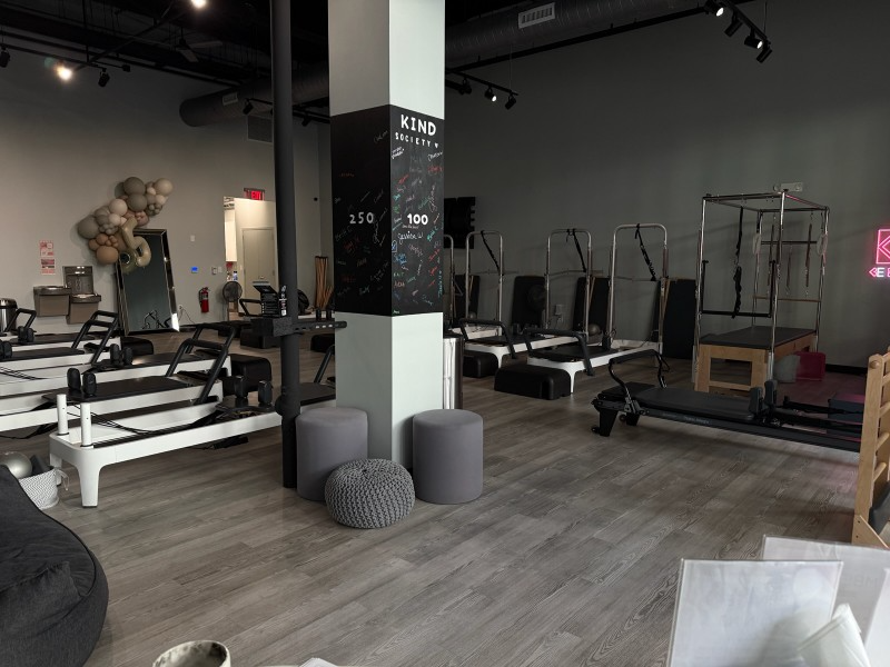 Pilates studio: exercise machines, gray floor, white walls, a black column with text, and a sign in the back.