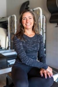 A woman is sitting on a pilates machine and smiling.