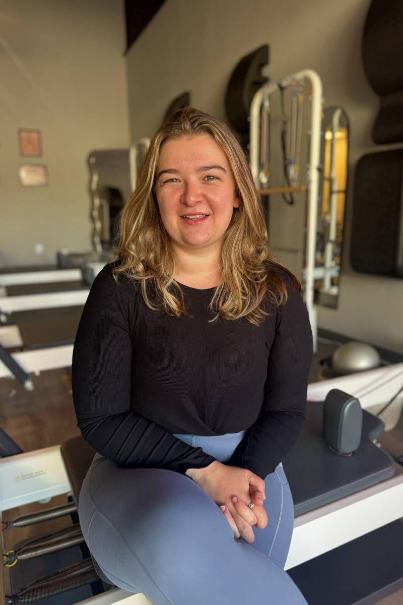 A woman is sitting on a pilates machine and smiling.