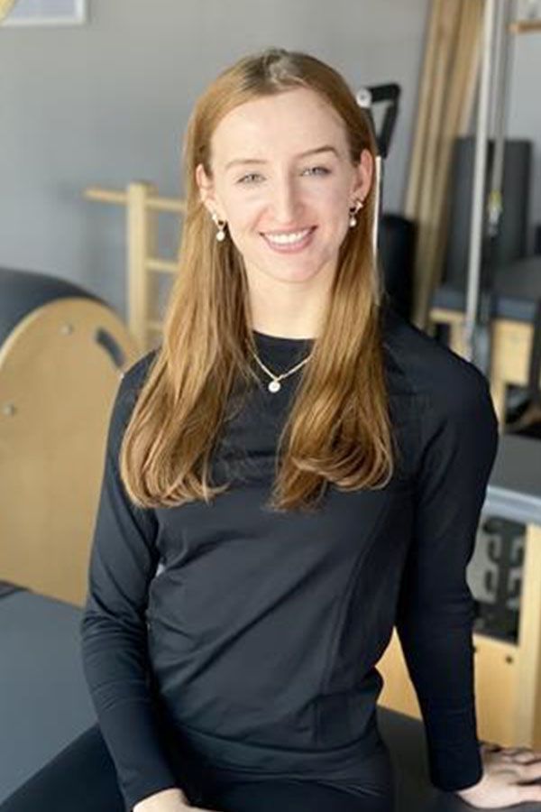 A woman is sitting on a pilates machine and smiling.