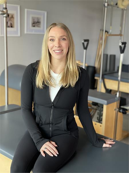 A woman is sitting on a pilates machine in a gym.