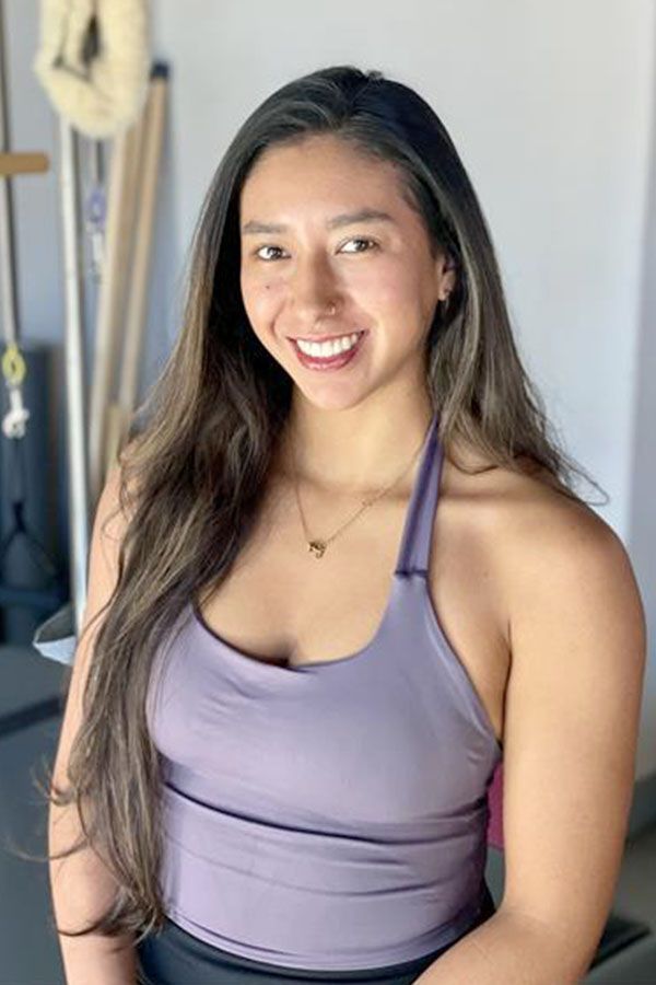 Woman in purple halter top smiling at the camera in a Pilates studio