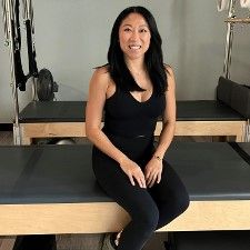 A woman is sitting on a pilates mat in a gym.