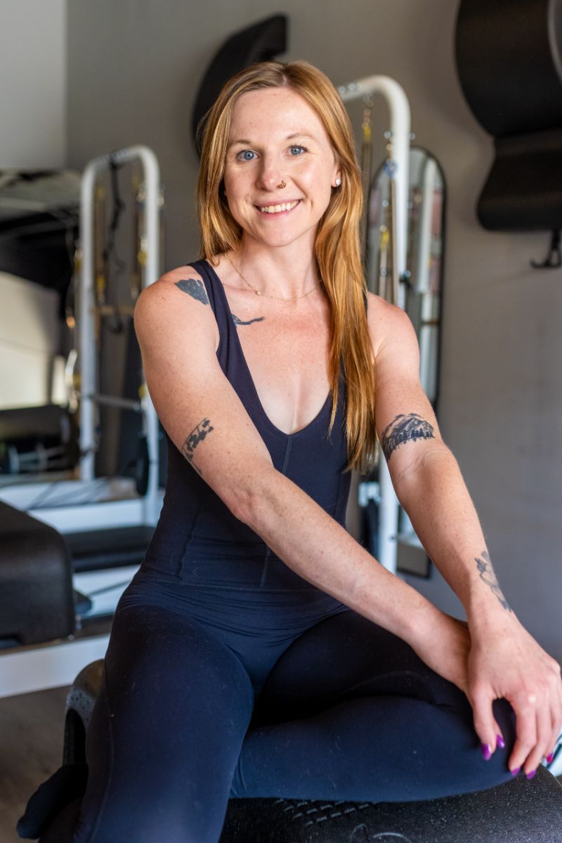 A woman is sitting on a pilates machine in a gym.
