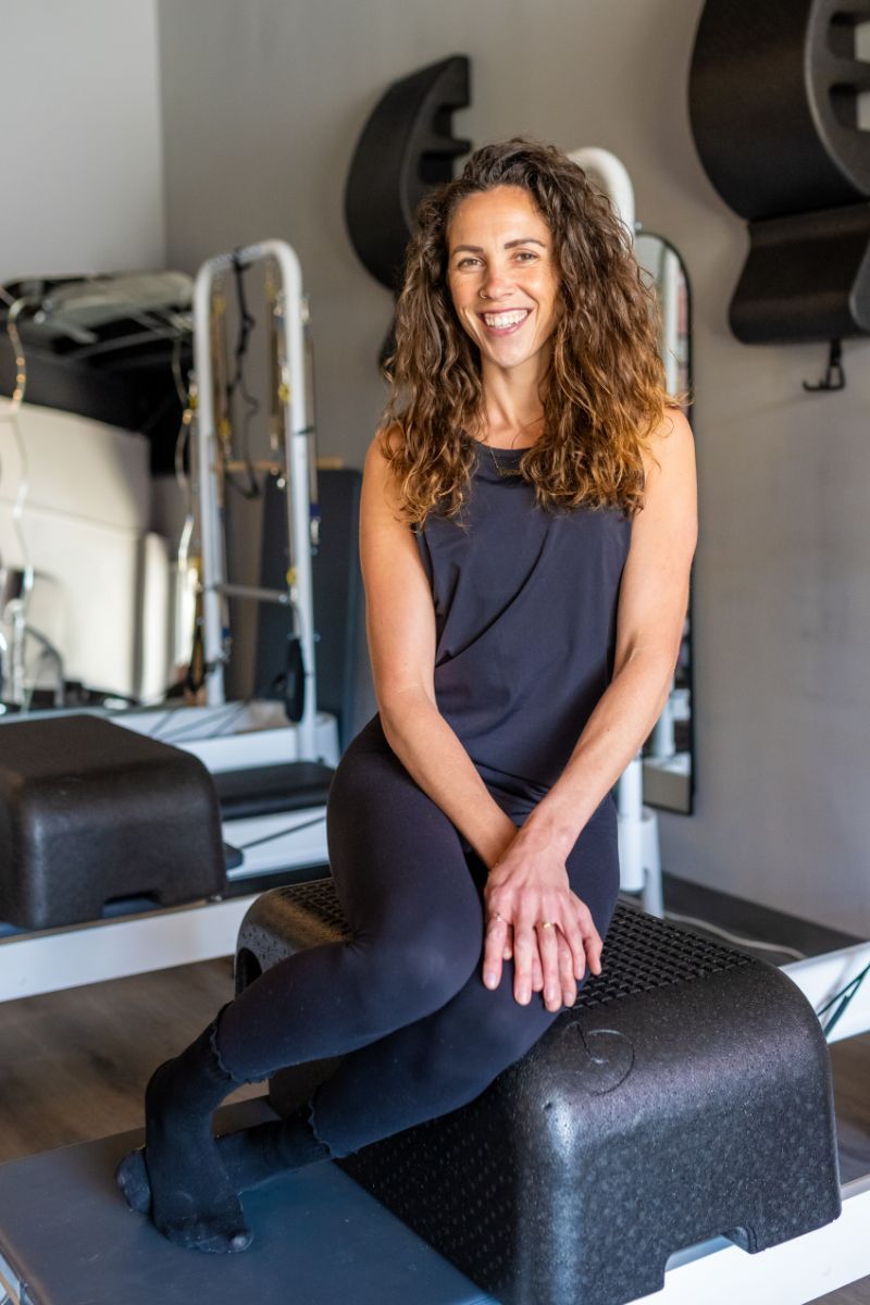 A woman is sitting on a pilates machine in a gym.