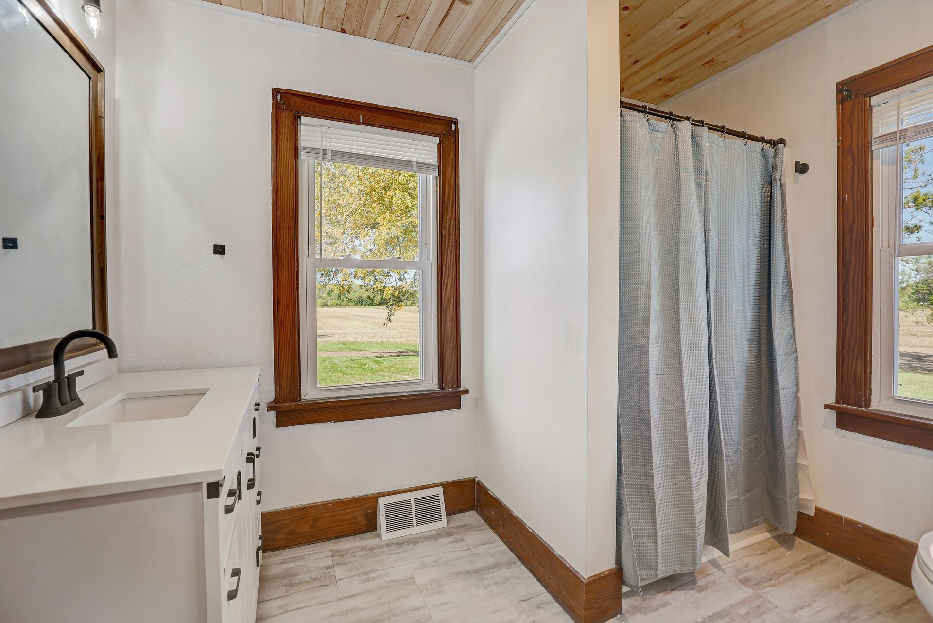 Bathroom with wood trim, a white vanity, shower curtain, and a window with an outdoor view.