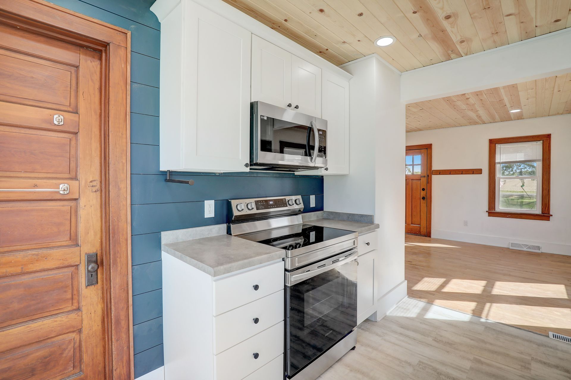 Kitchen with white cabinets, stainless steel appliances, blue wall, and wooden ceiling.