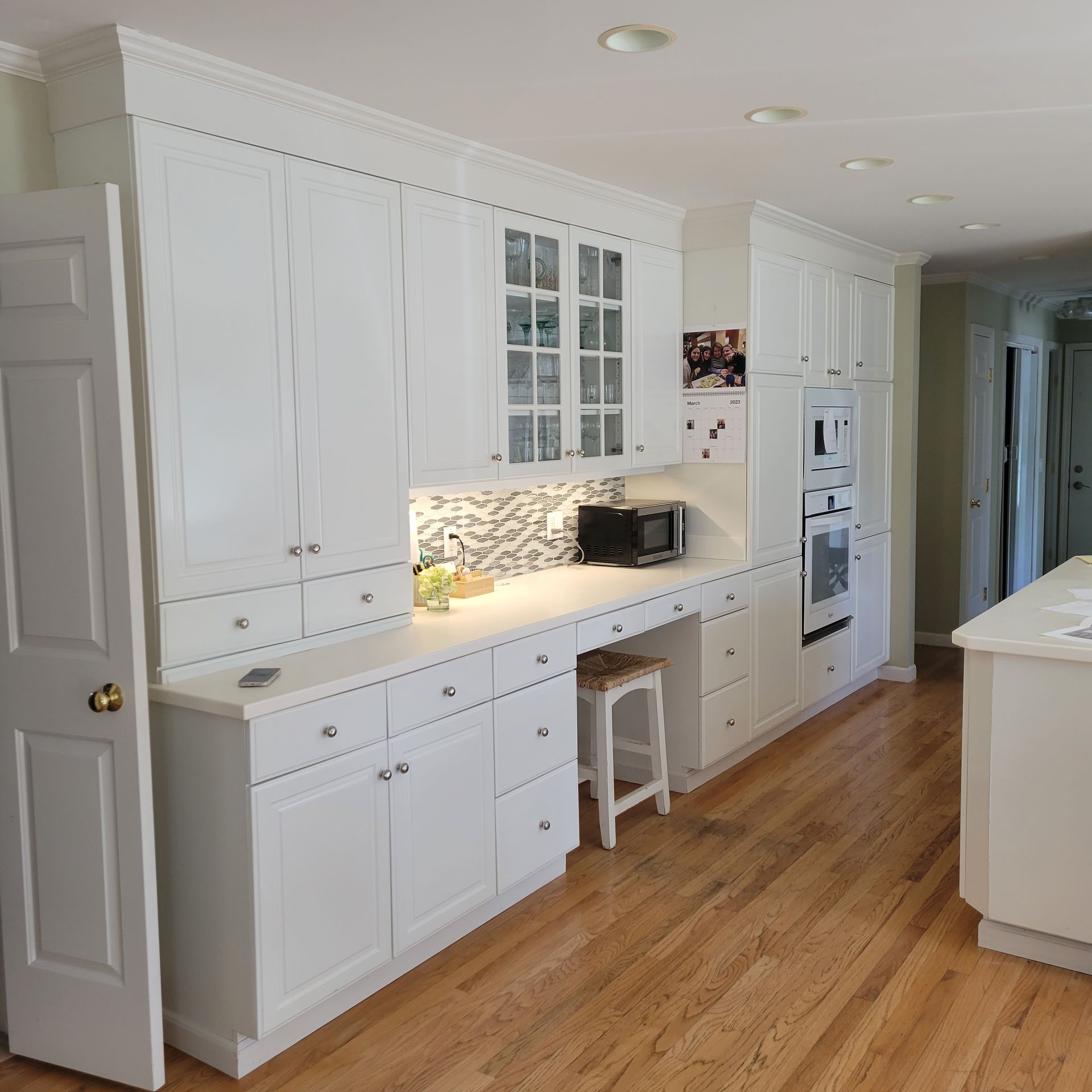 White kitchen with built-in cabinets, desk, microwave, and oven on a hardwood floor.