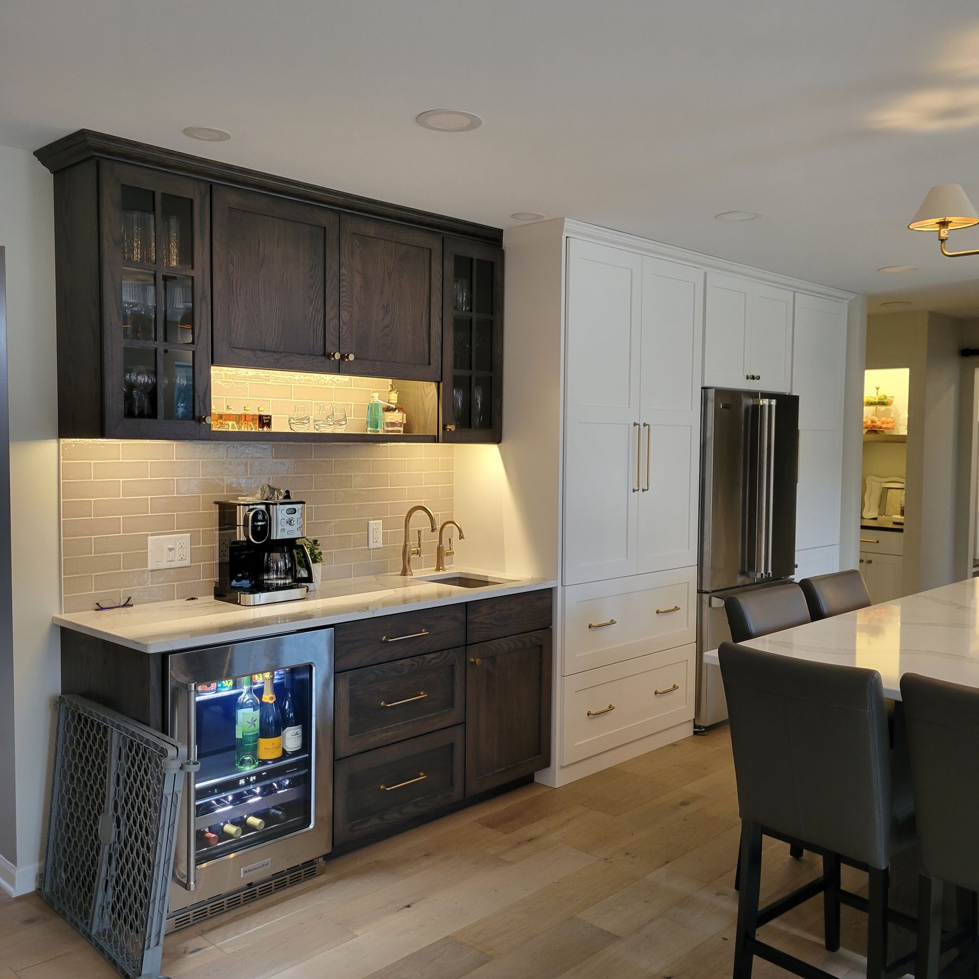 Kitchen bar area, built-in fridge, and white cabinetry next to stainless steel refrigerator and countertop with bar stools.
