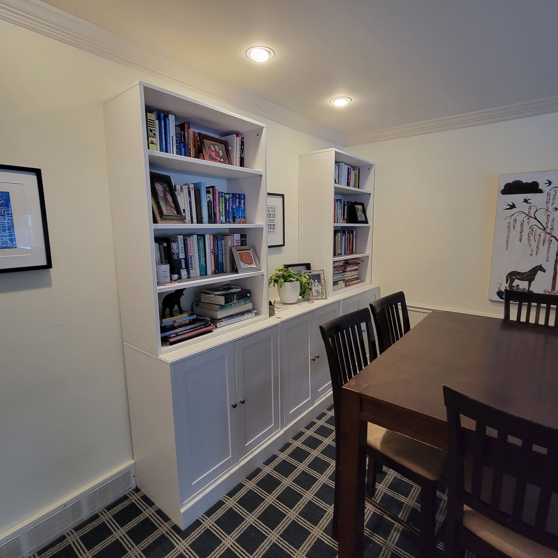 Built-in white bookshelves with books and decor flank a dining table with chairs in a room with artwork.