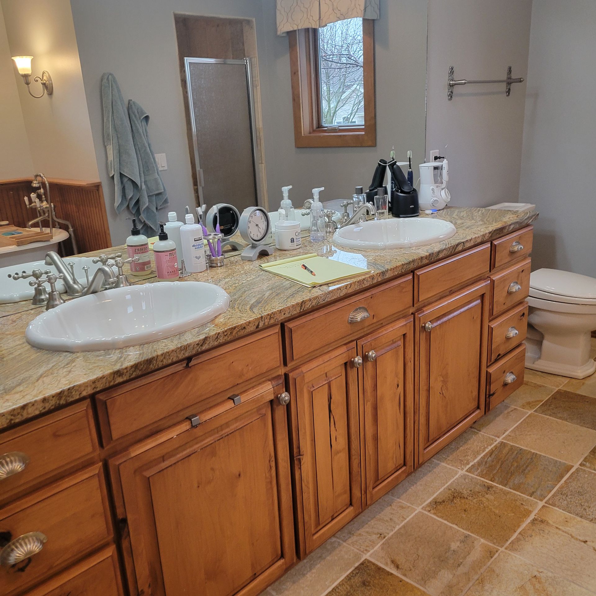 Bathroom with double sinks, granite countertop, wooden cabinets, and stone tile floor.