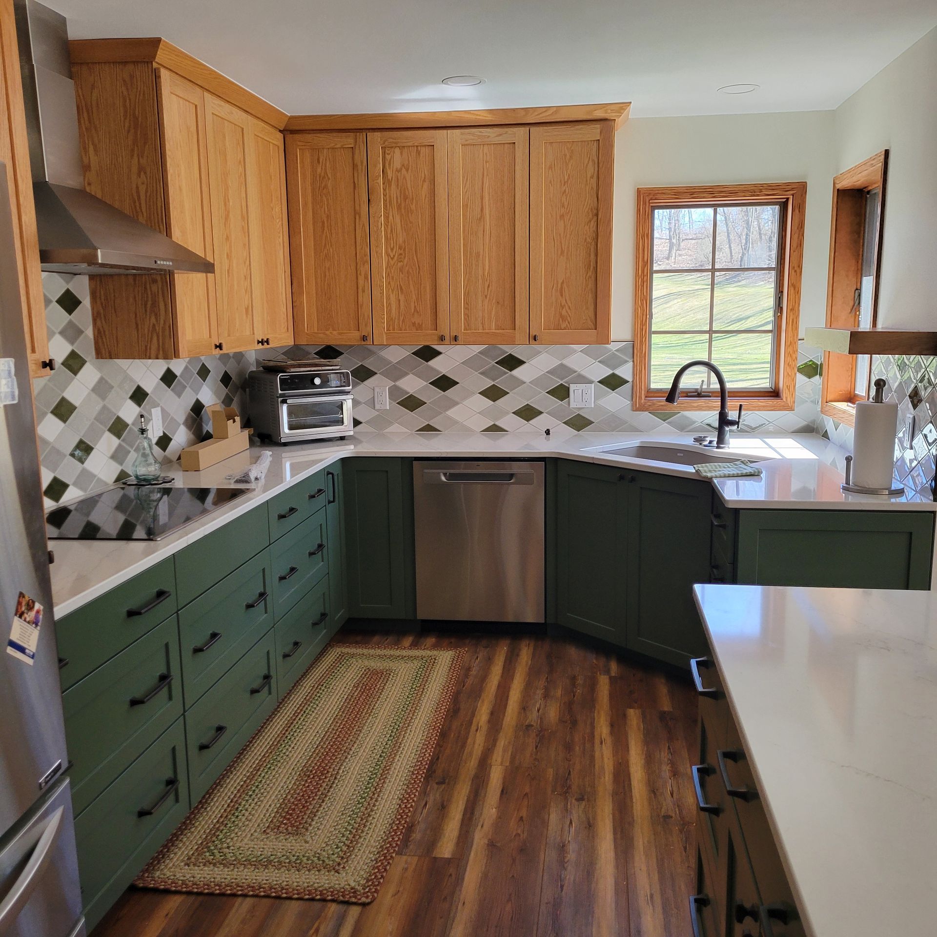 Green and wood-toned kitchen with green lower cabinets, light upper cabinets, white countertops, and a tiled backsplash.