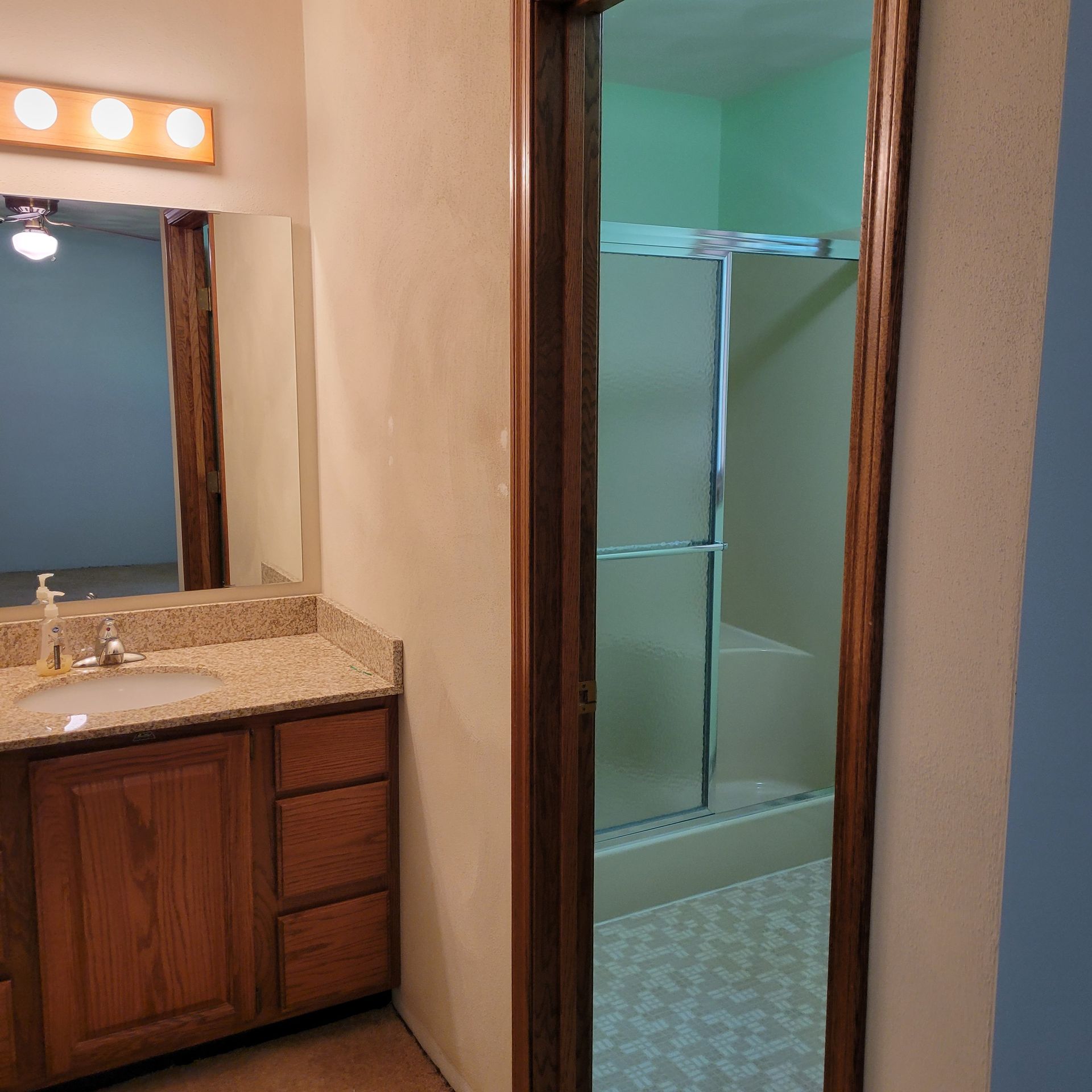 Bathroom interior with vanity, mirror, and shower visible through doorway.