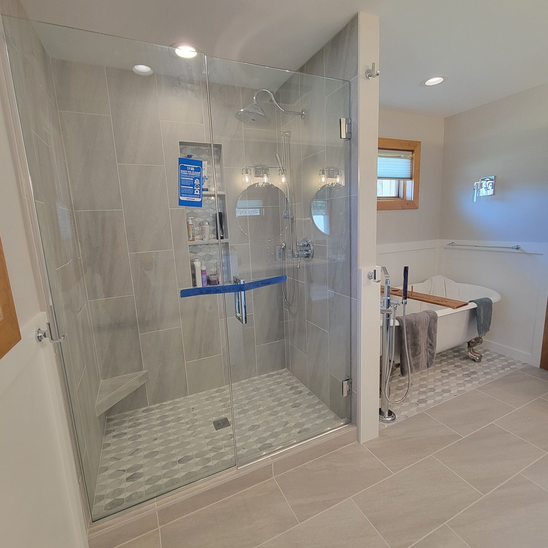 Modern bathroom with glass shower, gray tile, and a freestanding bathtub.
