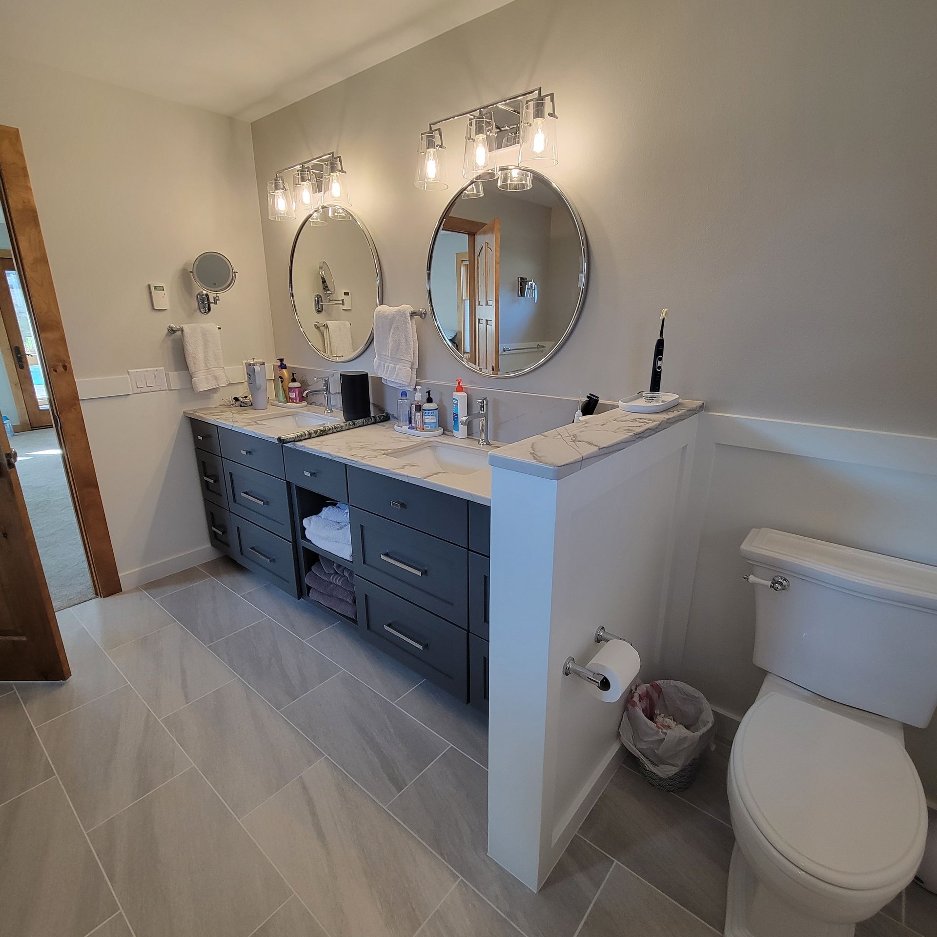 Bathroom with a gray double vanity, round mirrors, and a white toilet.