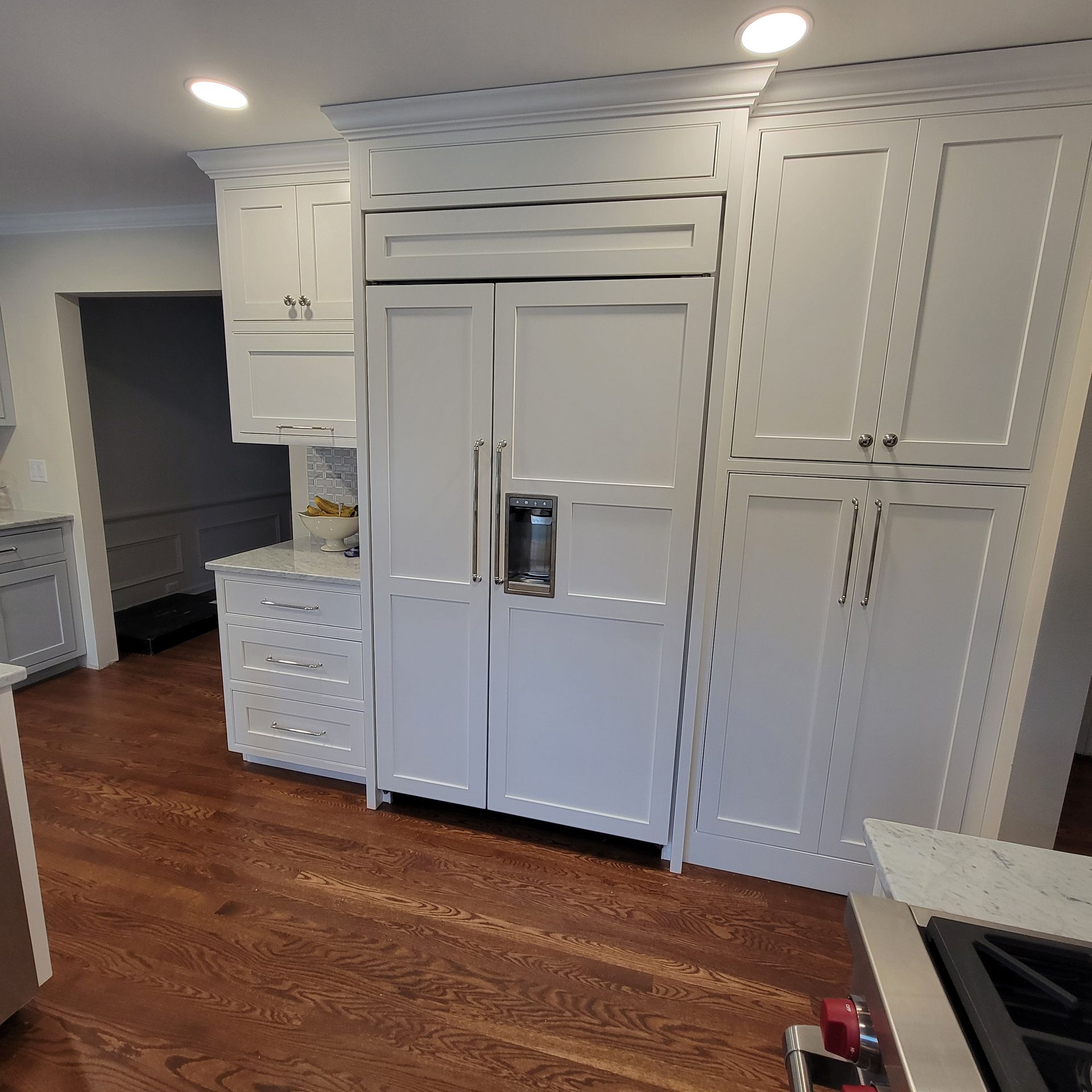 White kitchen with a large fridge, cabinets, and hardwood floor.