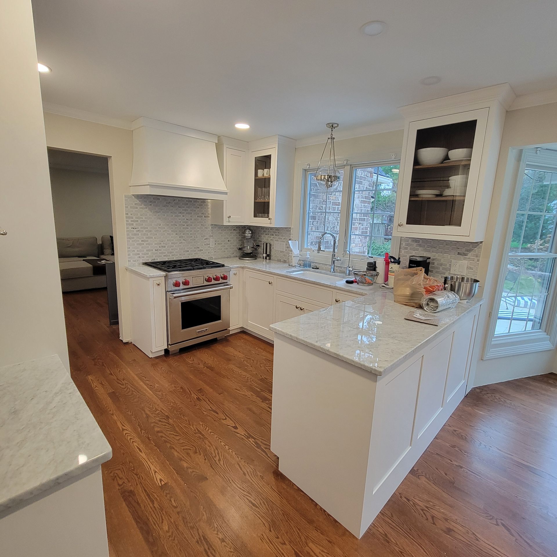 White kitchen with island, range, and cabinets. Hardwood floor and window.