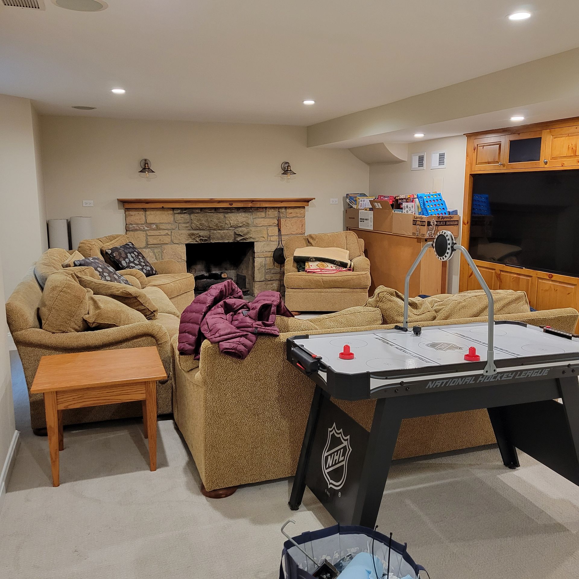 A messy basement with a couch, fireplace, air hockey table, and boxes.
