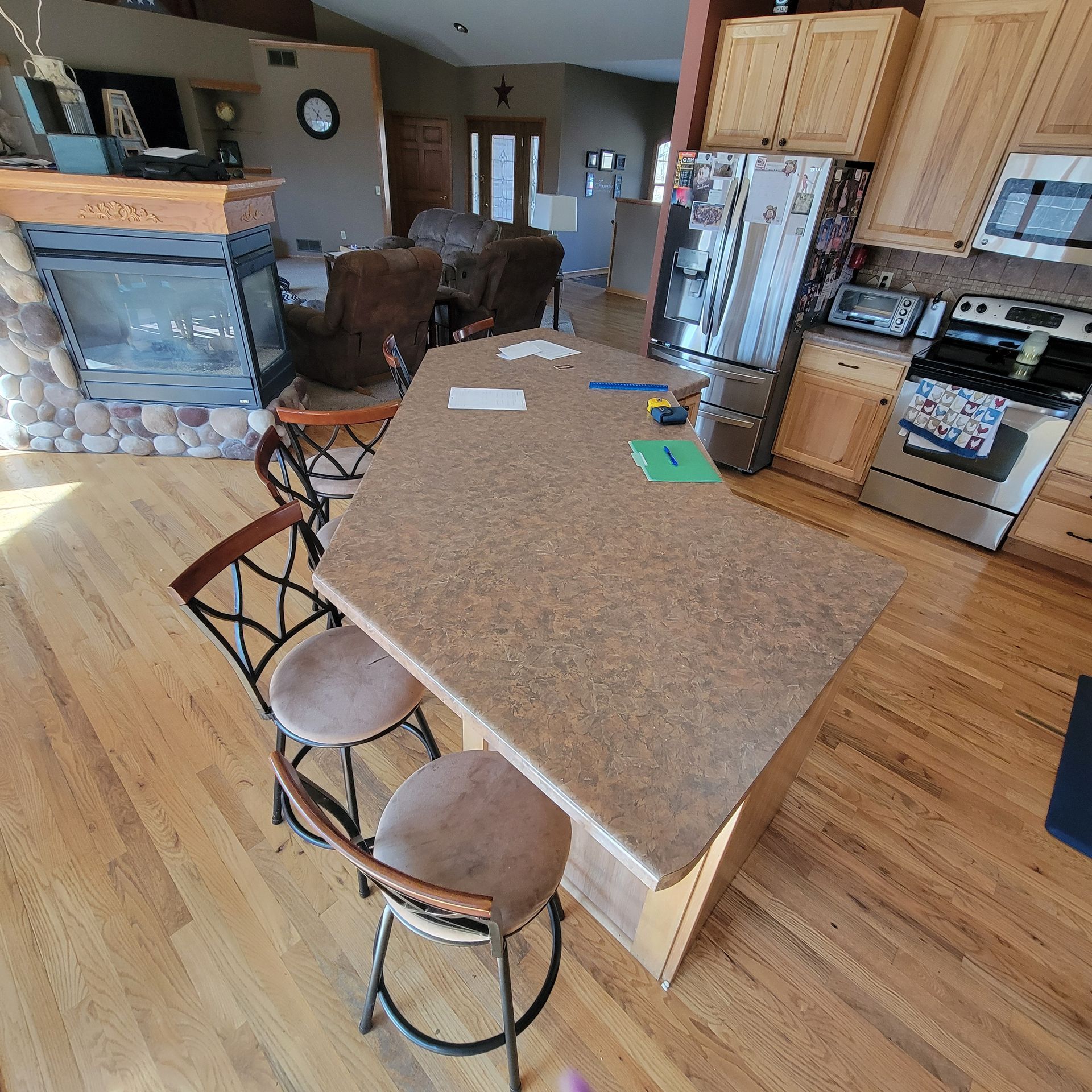 Kitchen with island, bar stools, and appliances; fireplace and living room in background.