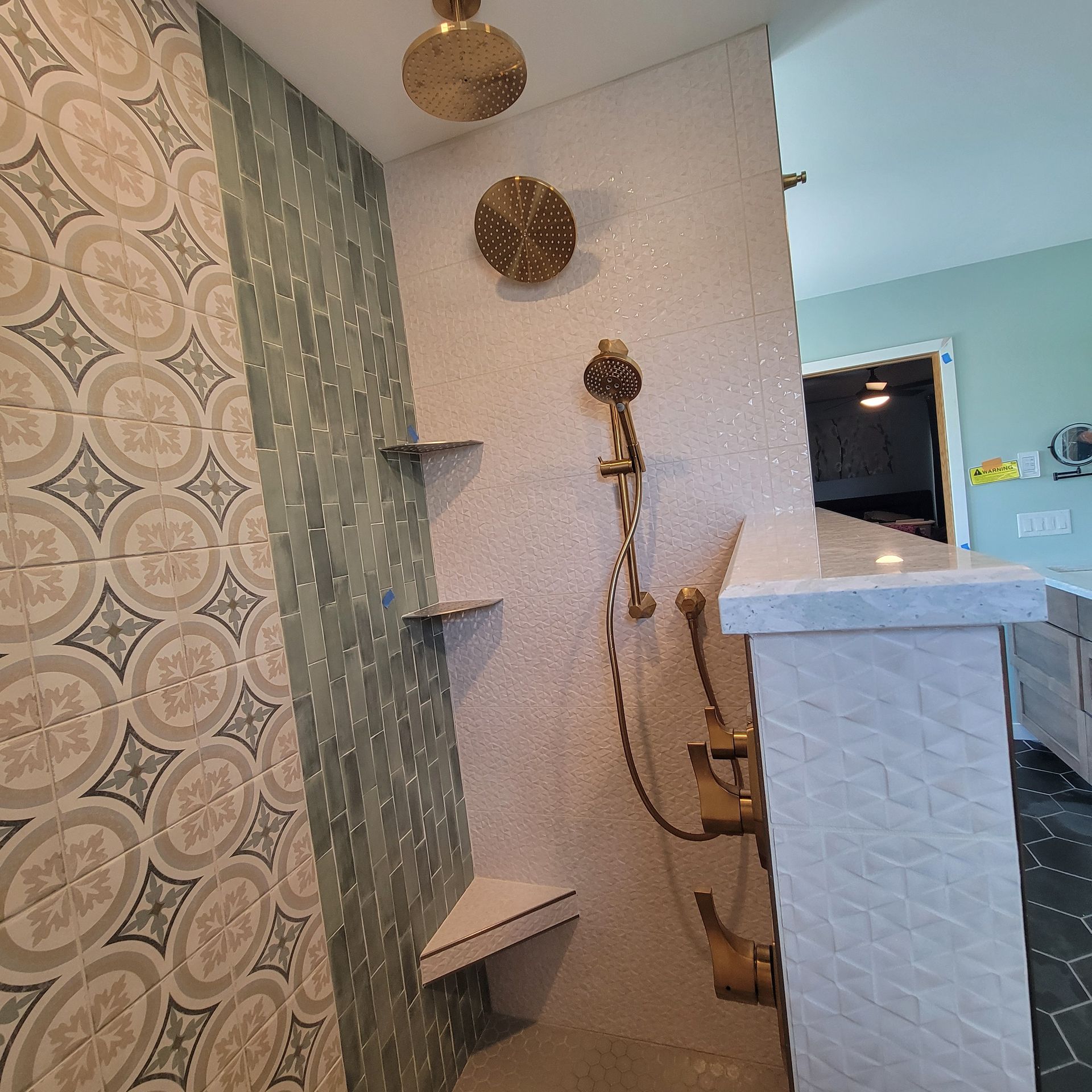 Shower with gold fixtures, mosaic tile, and built-in shelves, next to a patterned tiled wall.