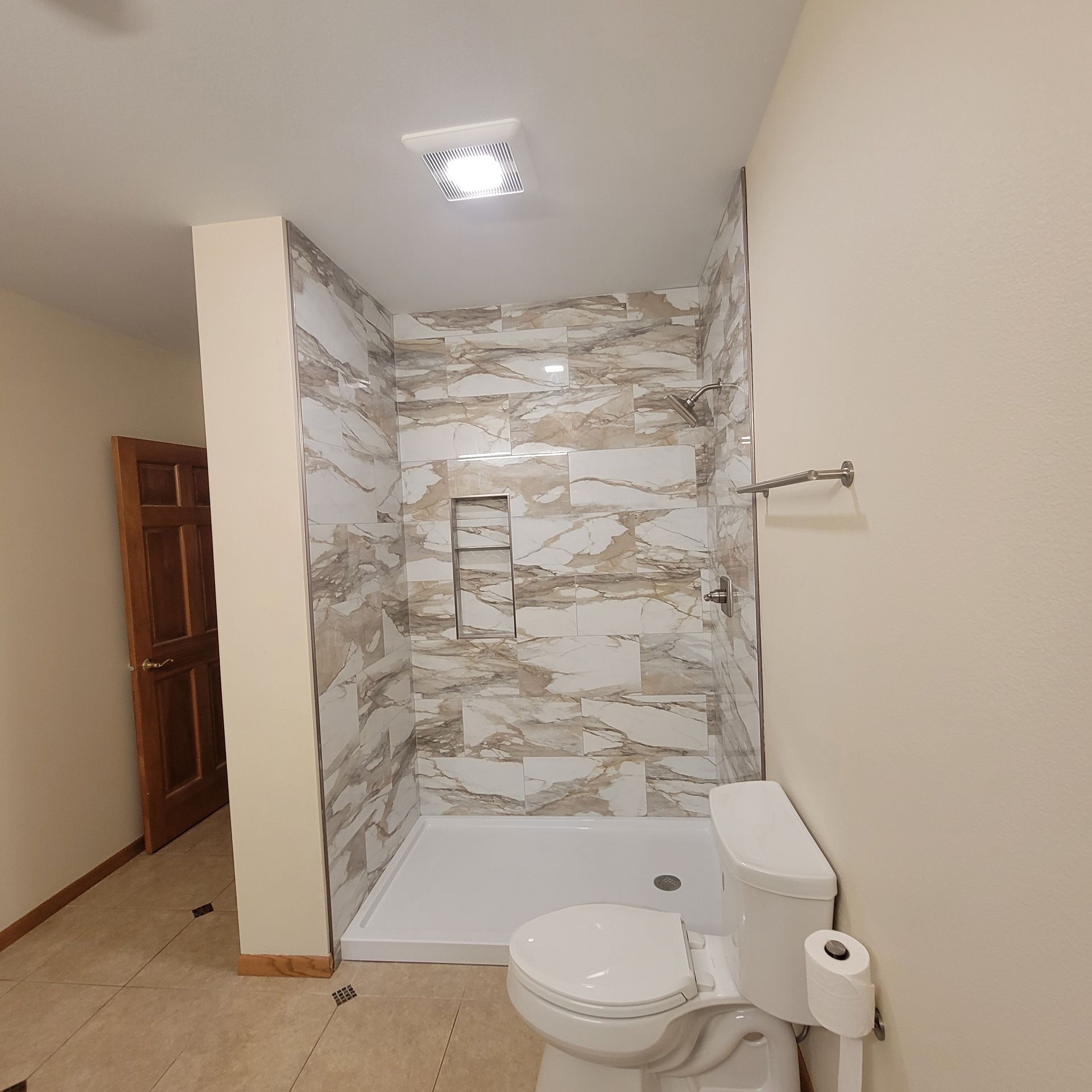 Bathroom with a tiled shower, toilet, and towel rack. The walls are beige. A wooden door is visible.