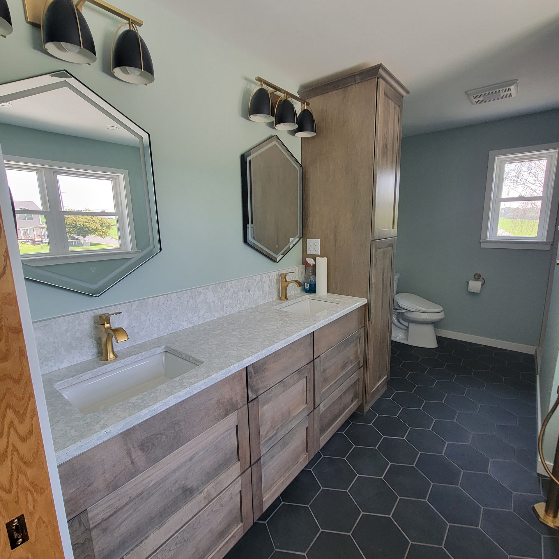 Bathroom with double vanity, hexagon tile floor, blue walls, and natural wood accents.