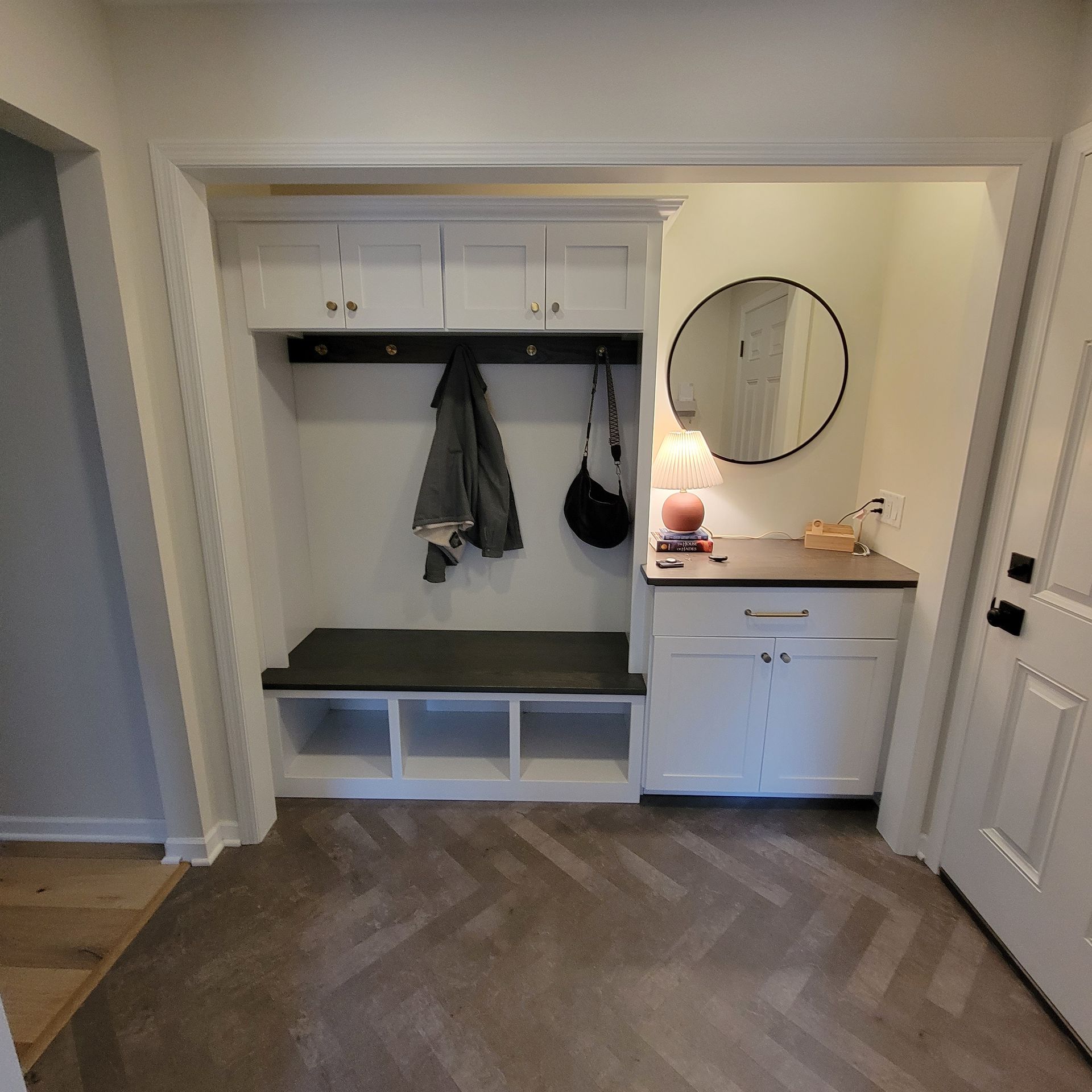 Hallway with built-in white cabinets, bench, and coat hooks. Includes a mirror, table, and door.