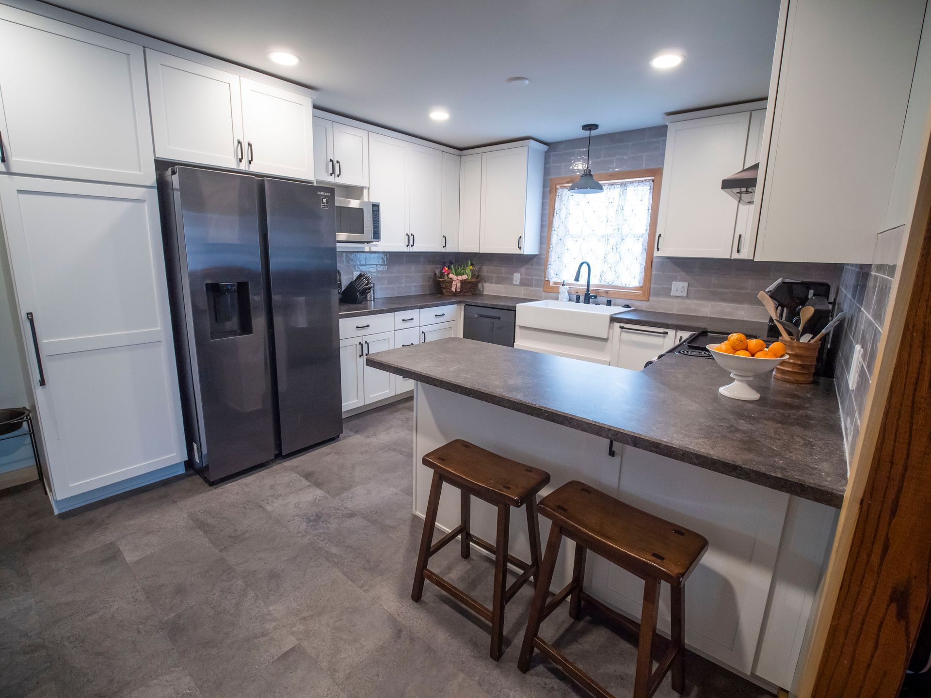 White kitchen with gray countertops, stainless steel appliances, and two brown stools.