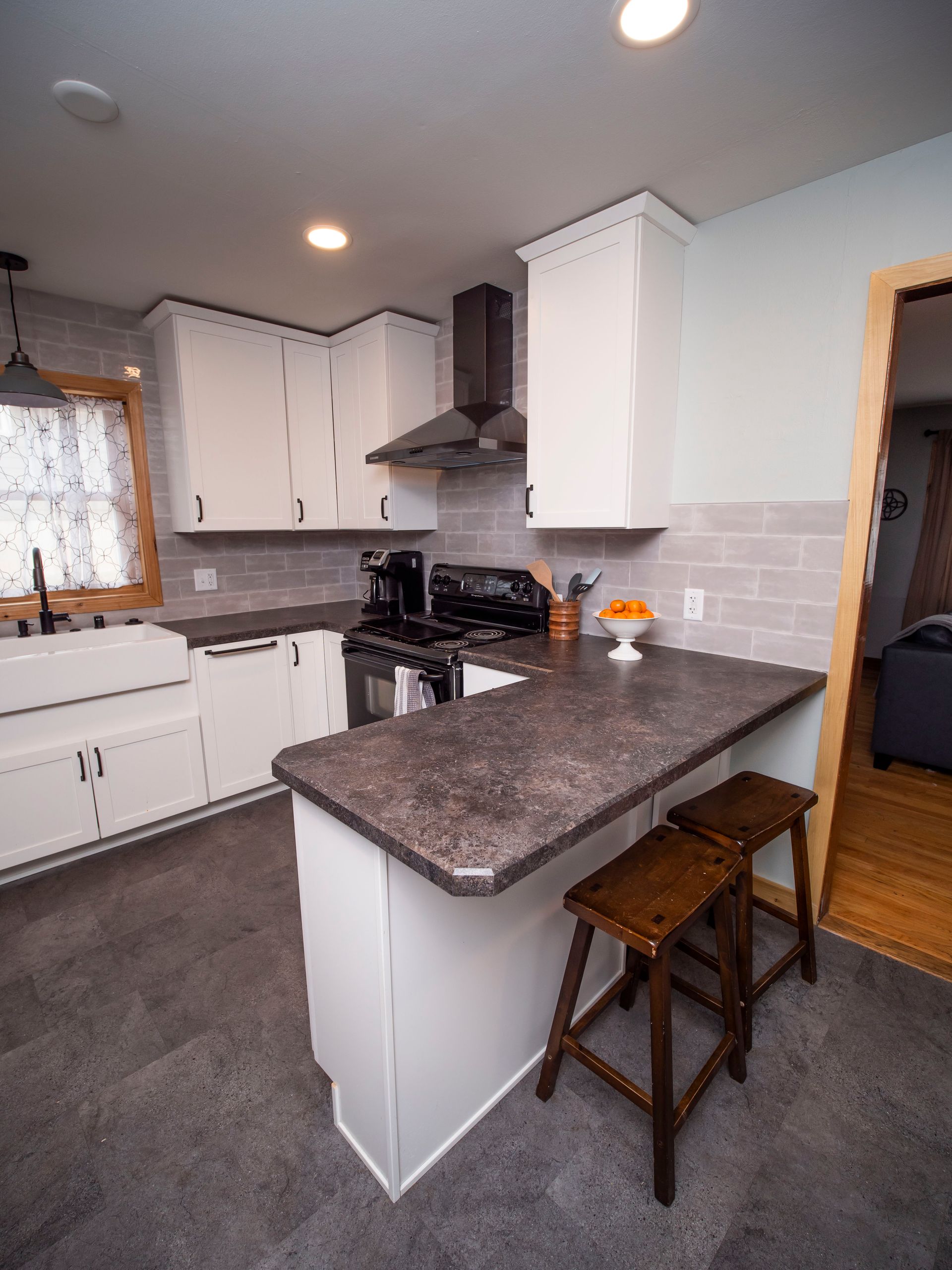 Modern kitchen with white cabinets, dark countertops, a stove, and two wooden stools.