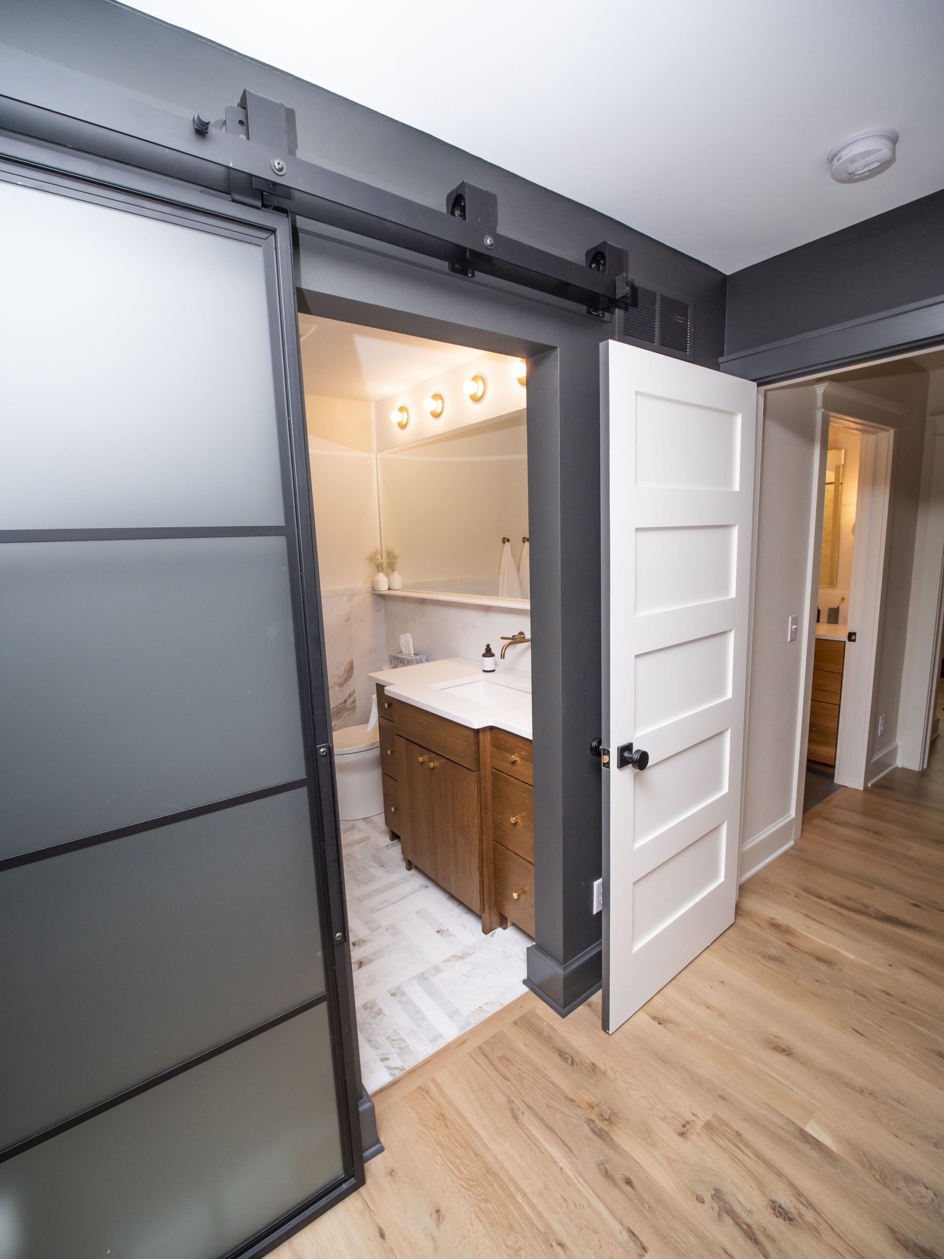 A bathroom entrance with a sliding frosted glass door and white interior door, light wood floors.