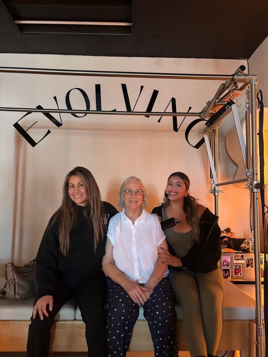 Three people seated indoors beneath an arched “EVOLVIA” sign, smiling at the camera