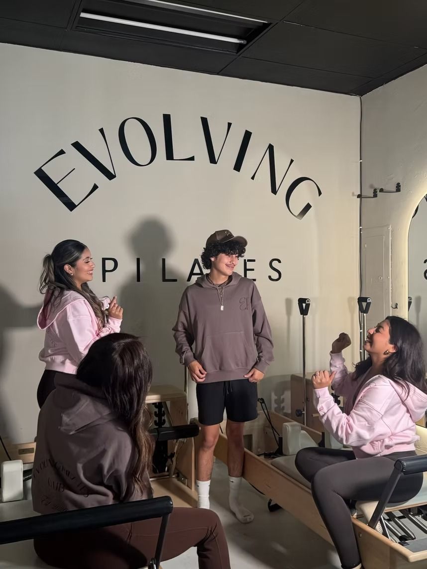 Group chatting in a Pilates studio with “EVOLVING PILATES” on the wall.