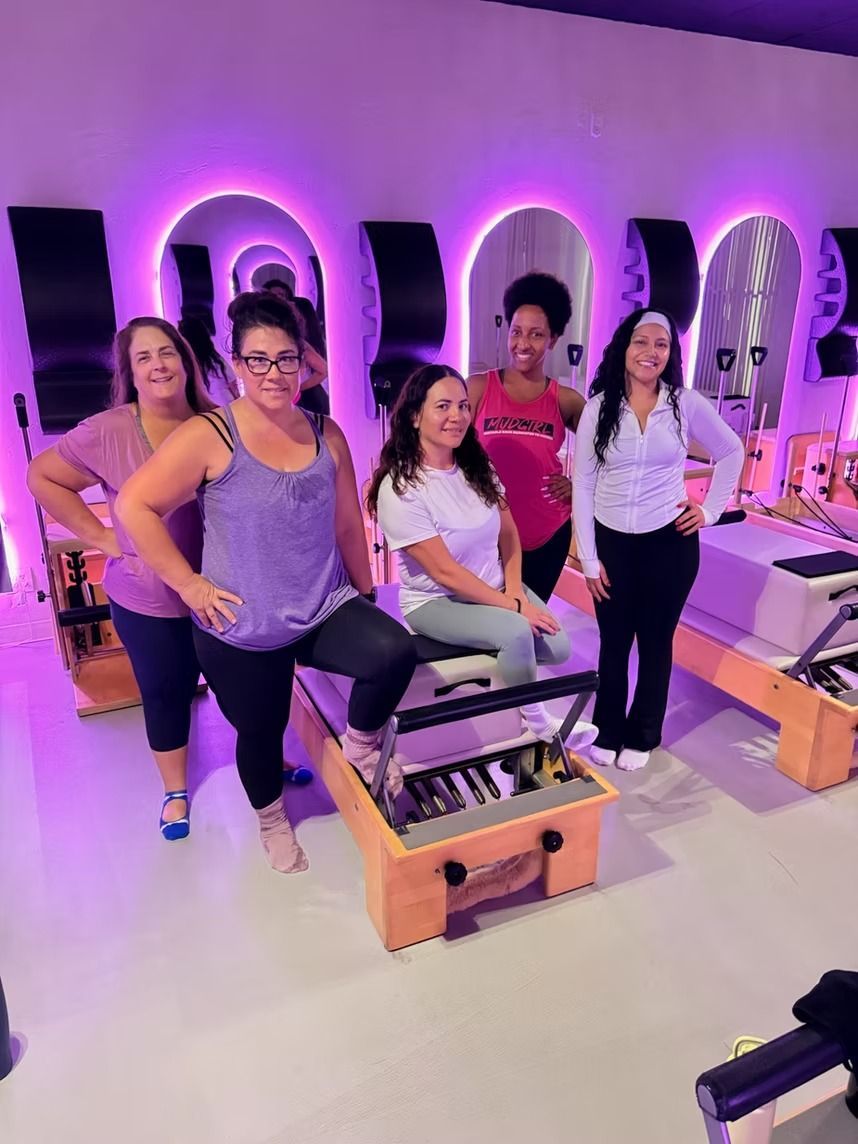 Group posing in a neon-lit fitness studio on exercise machines, smiling at the camera.