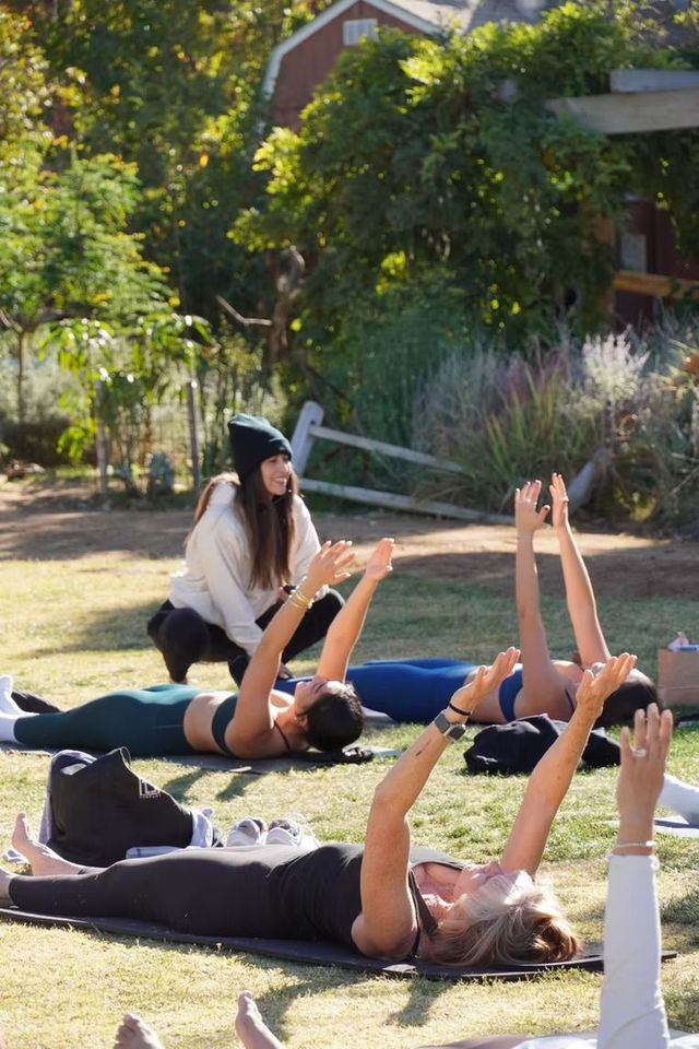 People doing a group yoga stretch on grass outdoors with an instructor nearby