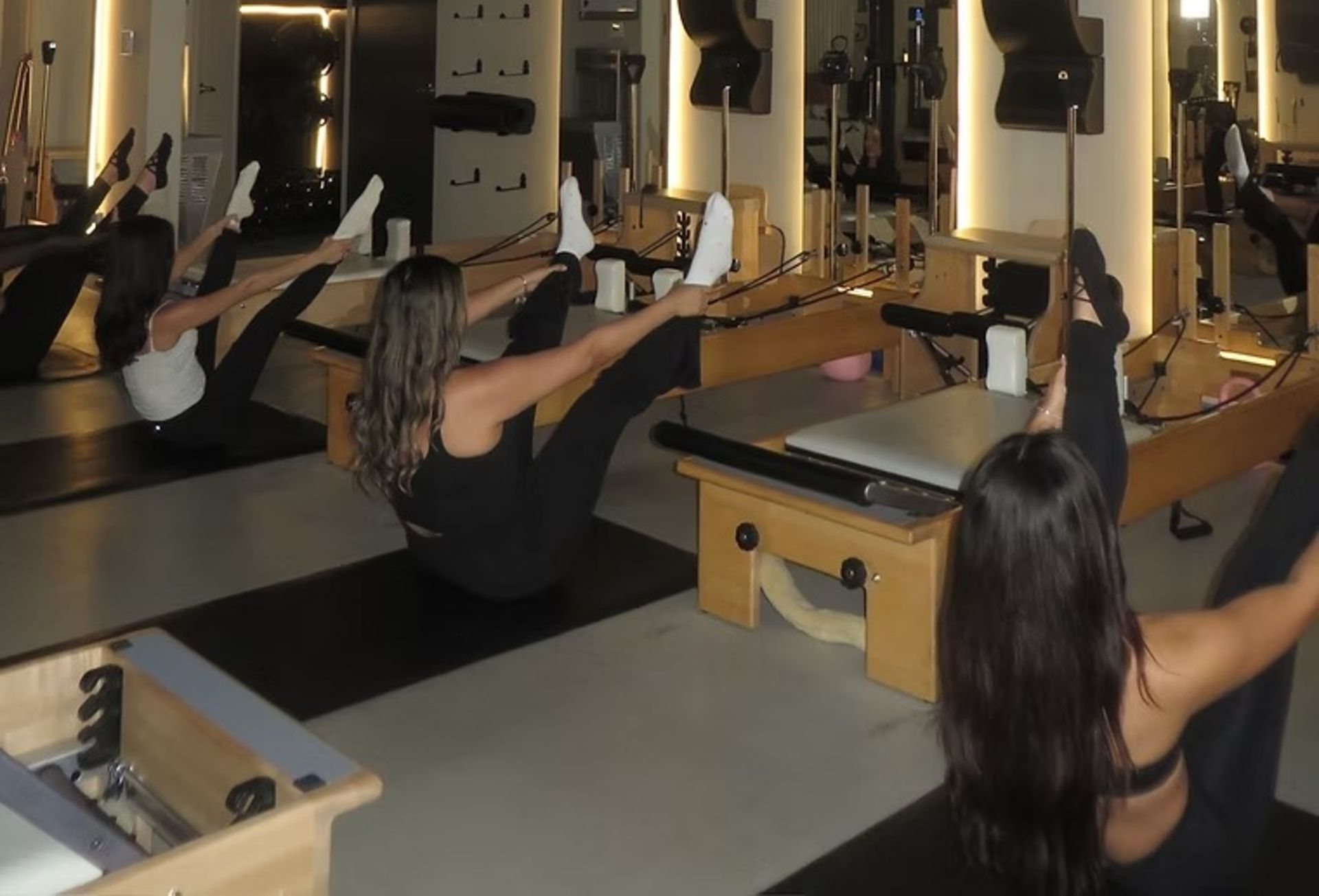 Pilates class on reformer machines in a mirrored studio, with people exercising in rows.