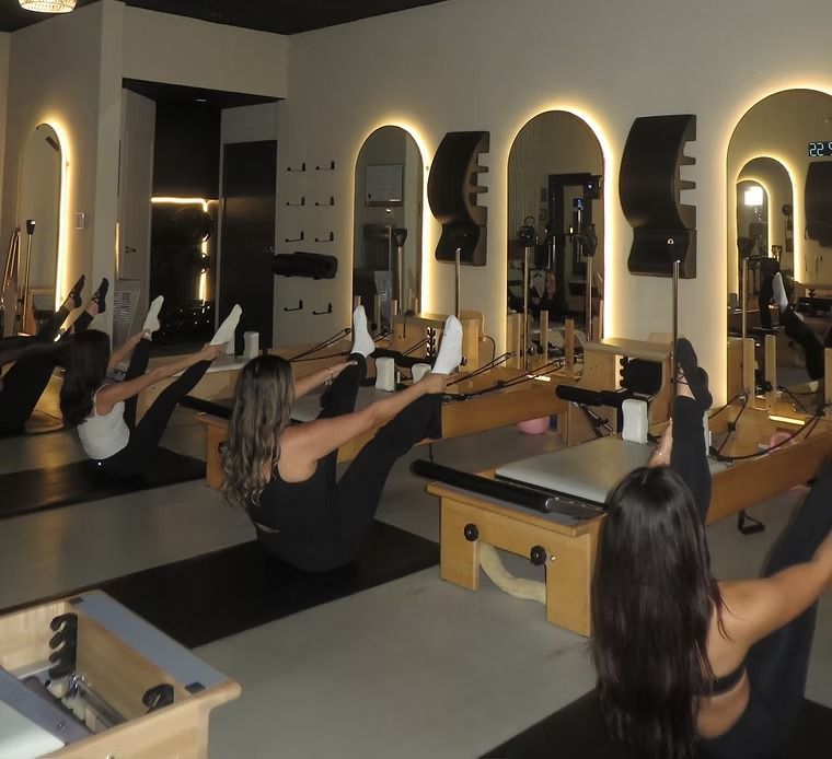 Pilates class on reformer machines in a mirrored studio, with people exercising in rows.