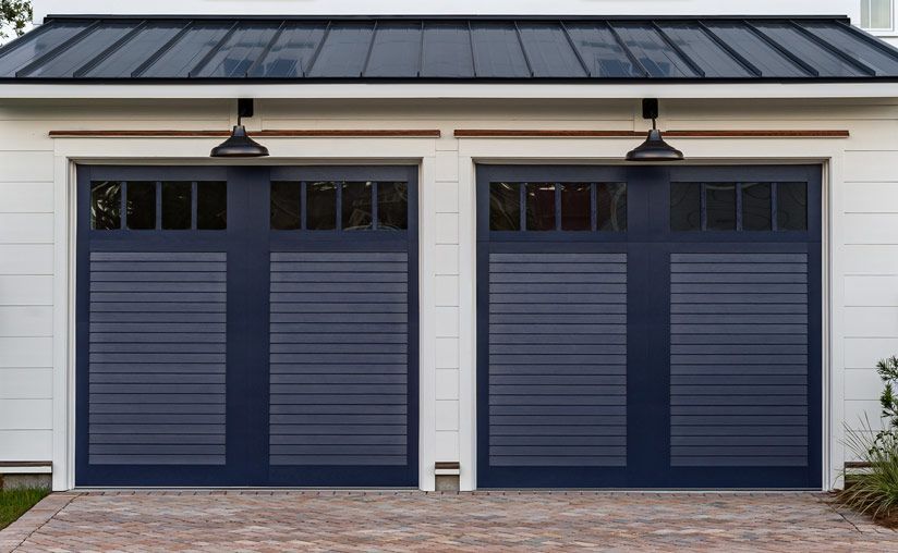 A white house with two blue garage doors and a black roof.