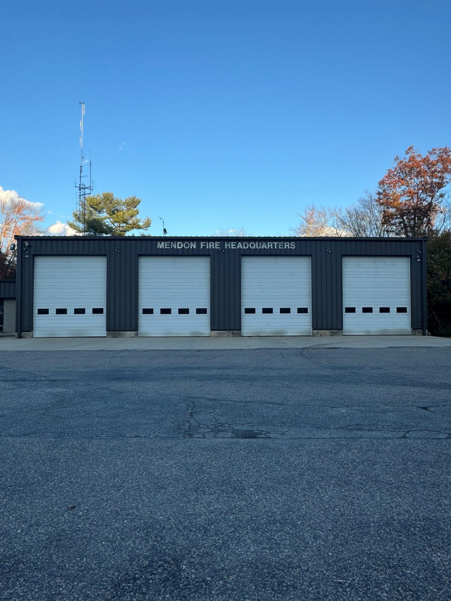 Dark gray fire station with four white garage doors, blue sky background.