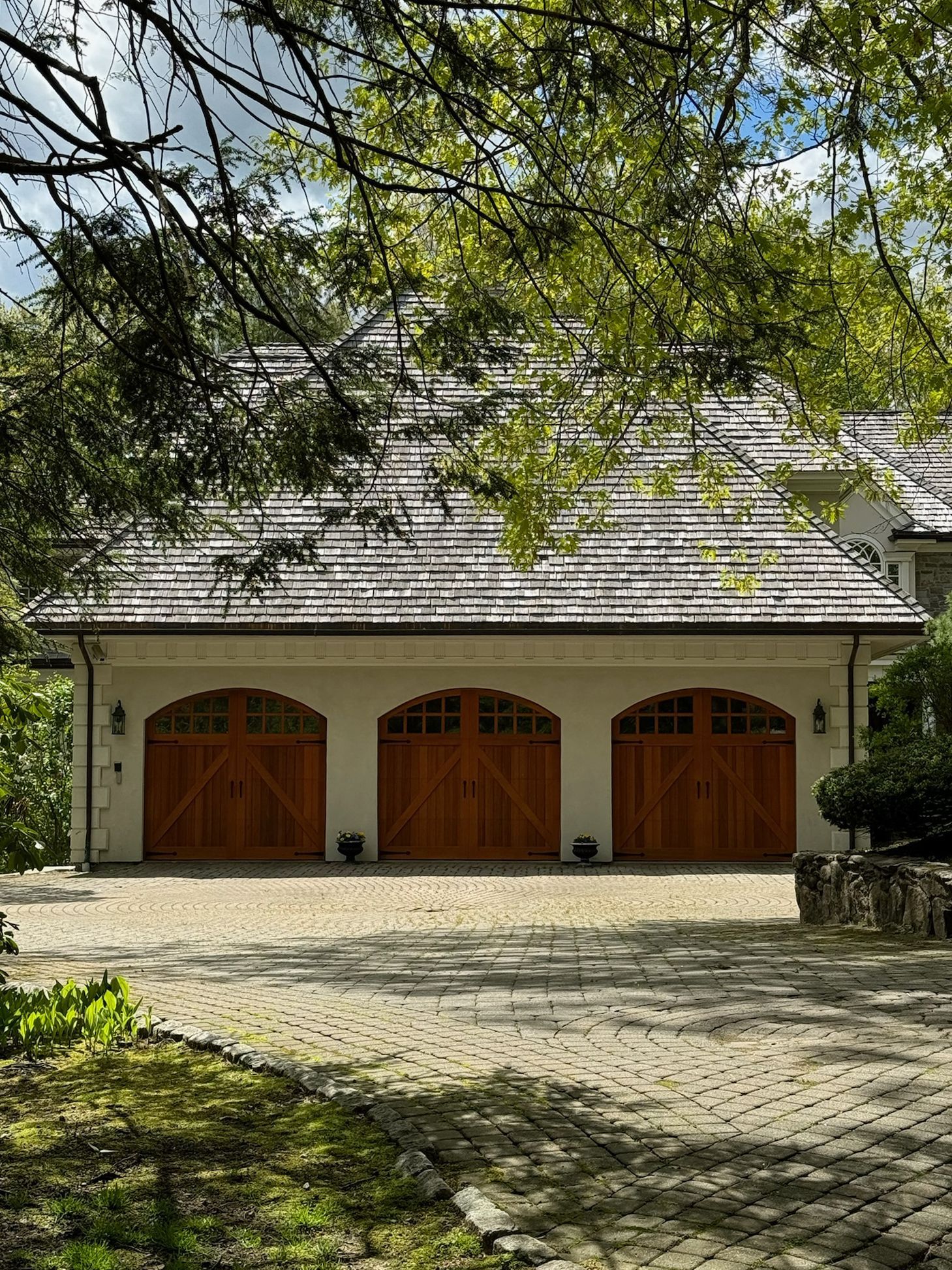 A large white house with three wooden garage doors and a shingle roof.