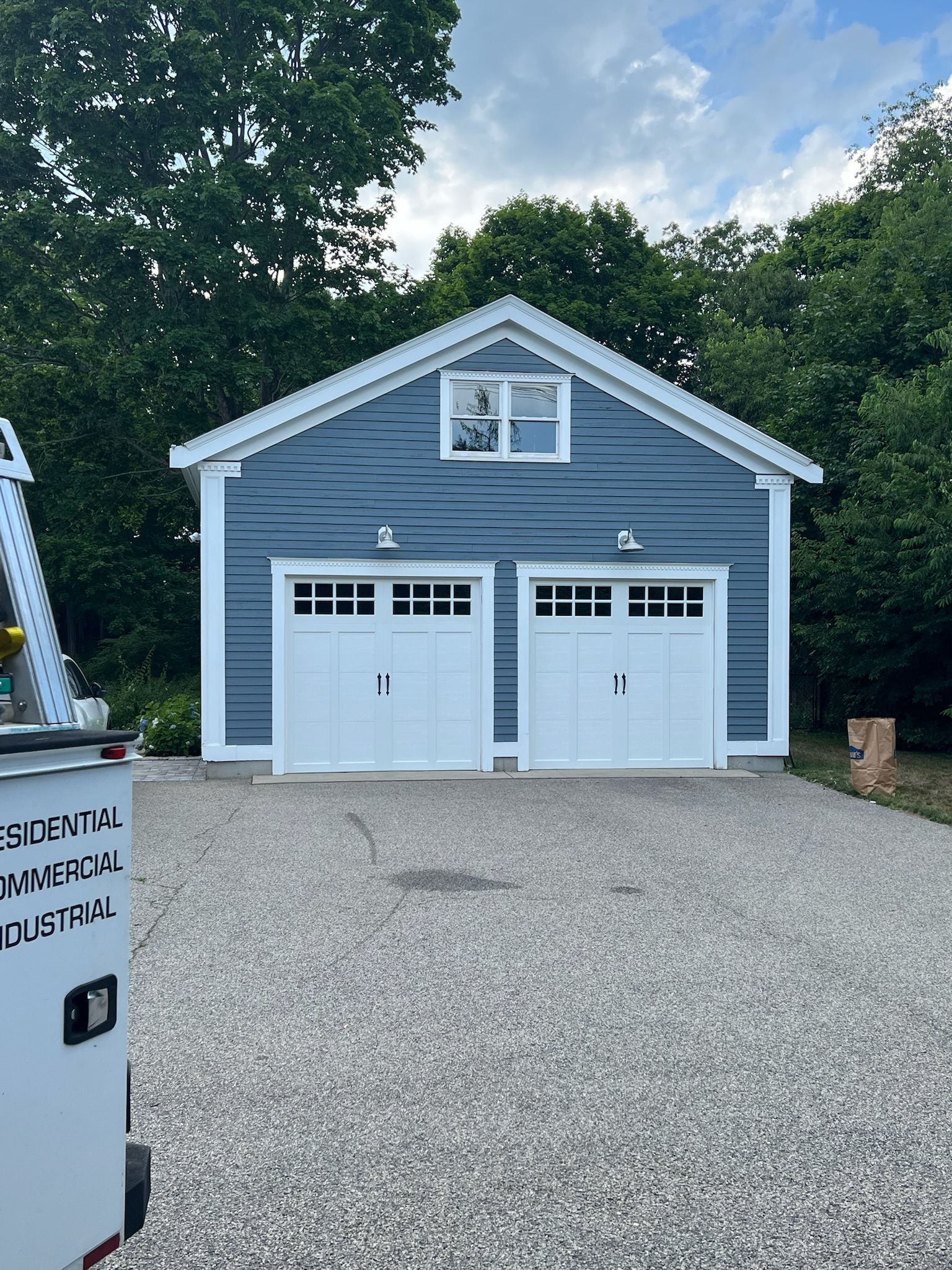 A blue garage with white doors and a white trailer parked in front of it.