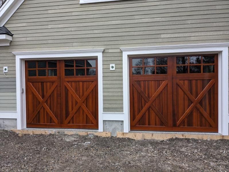 Two wooden garage doors are on the side of a house.