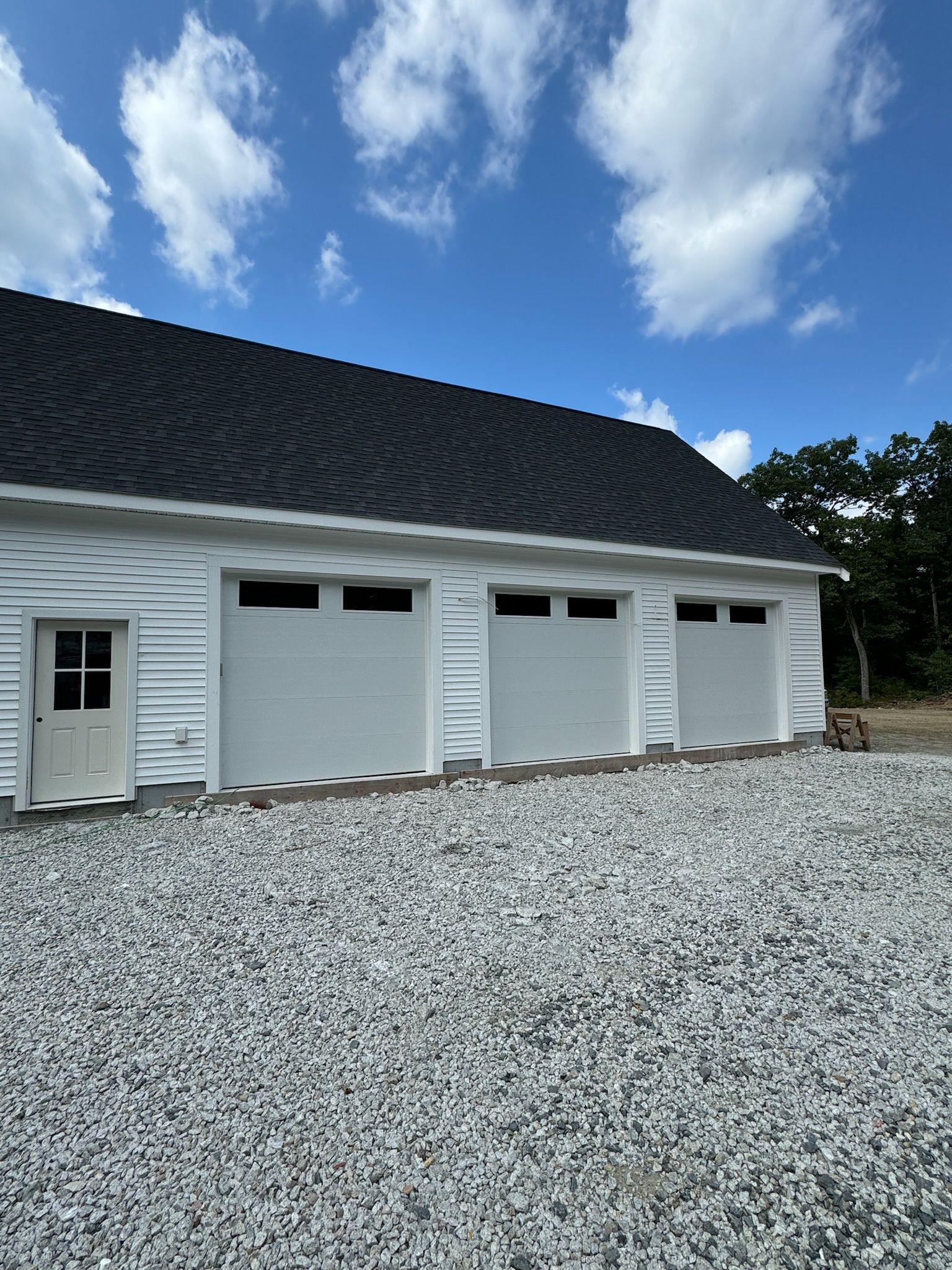 A white garage with three garage doors and a gravel driveway