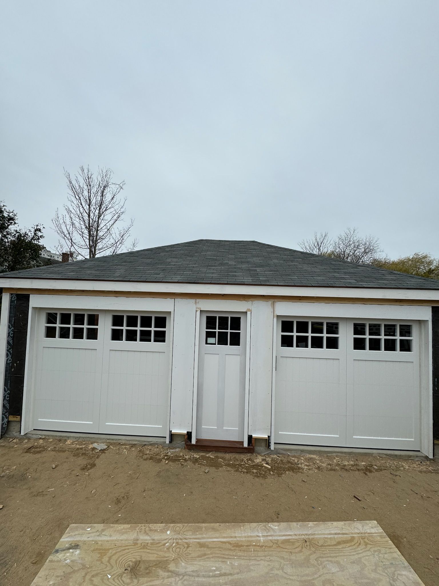 A garage with three white garage doors and a black roof