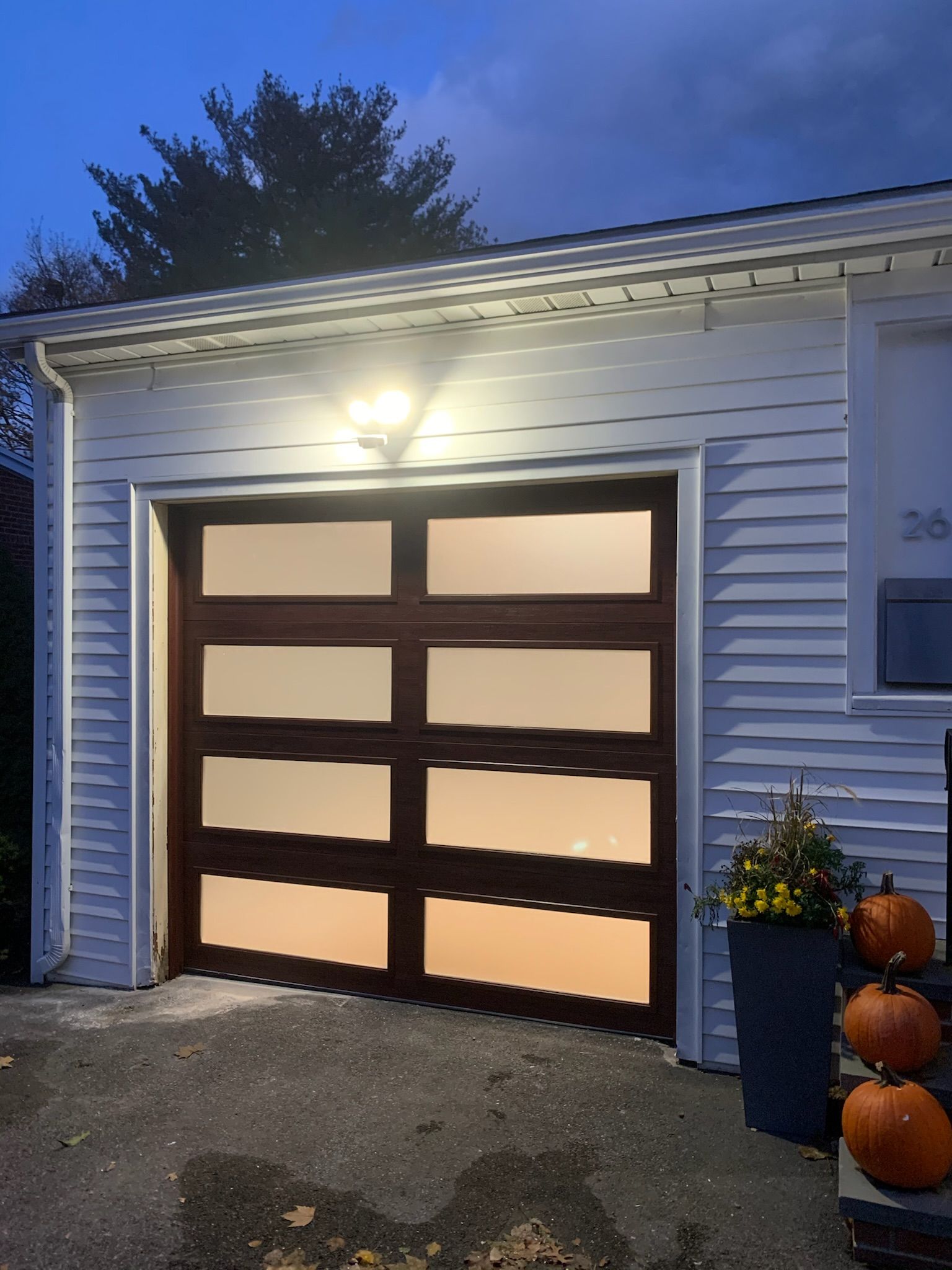 A white house with a brown garage door and pumpkins in front of it