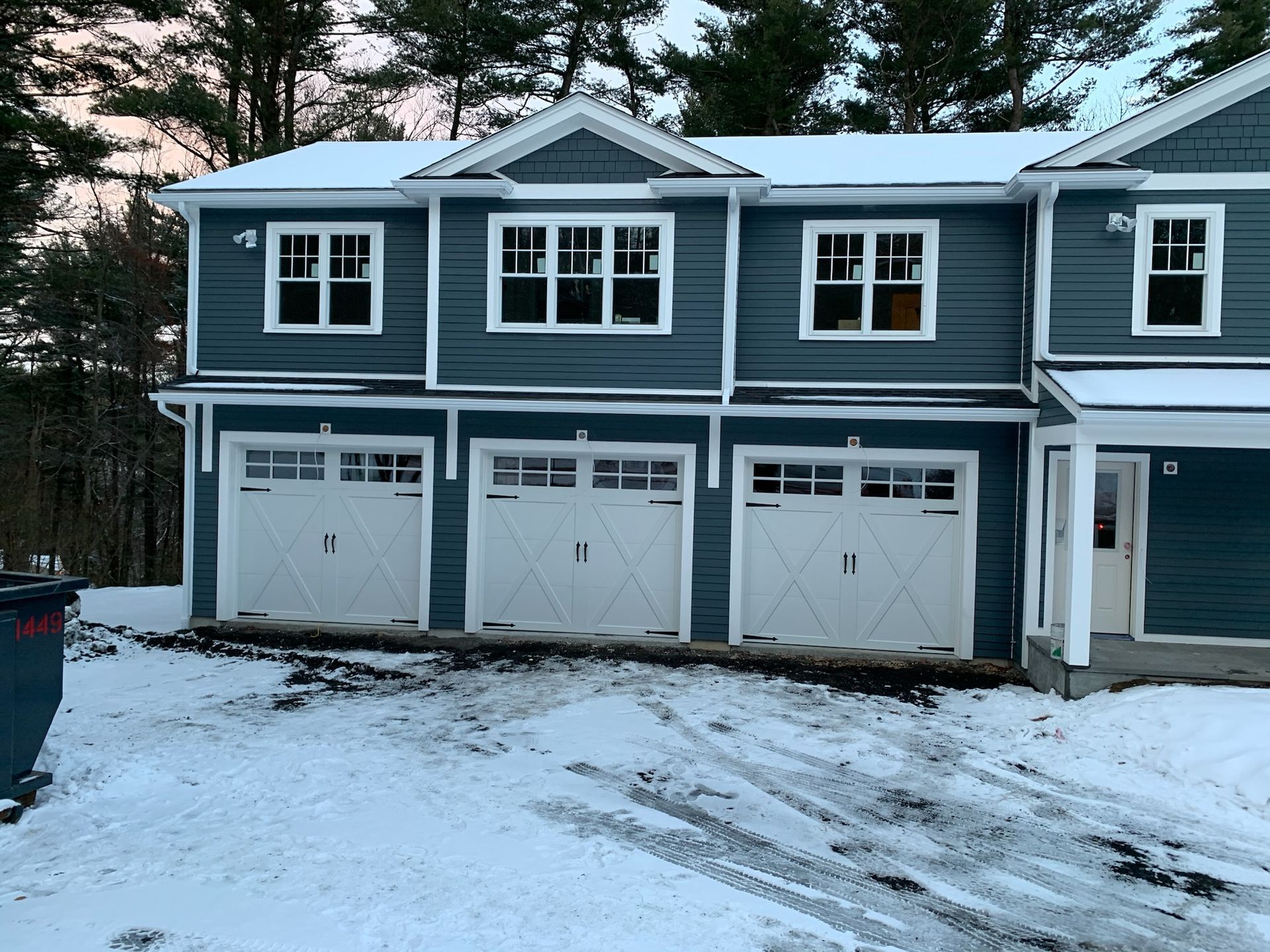 A blue house with white garage doors is covered in snow