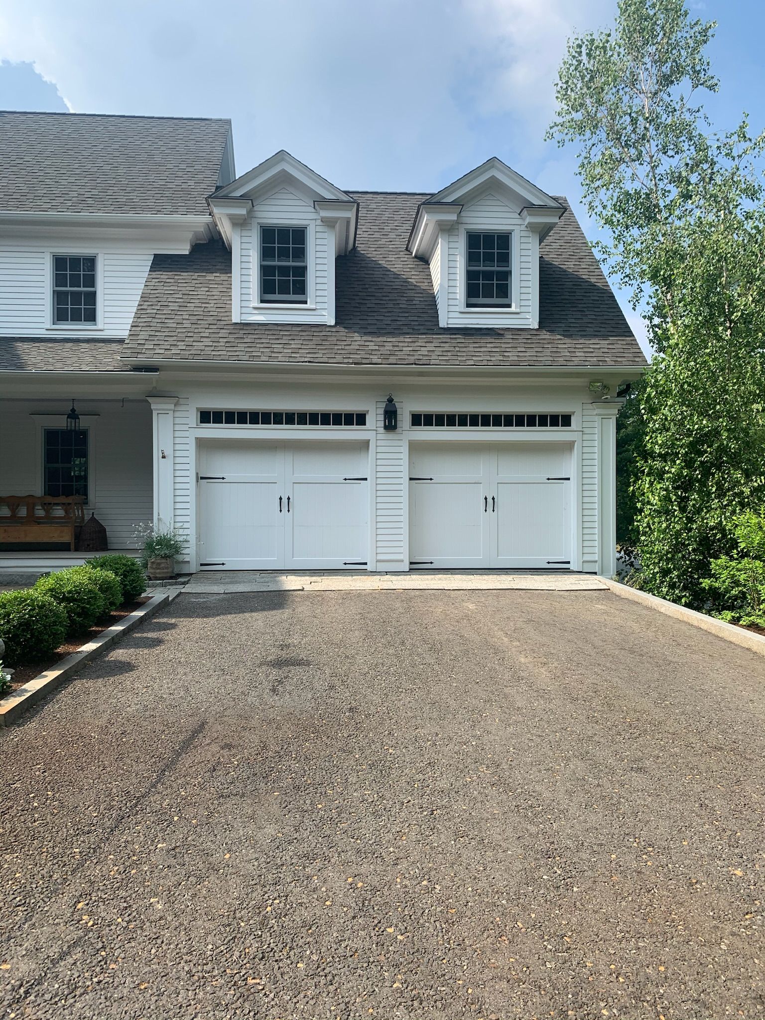 A white house with two garage doors and a gravel driveway.